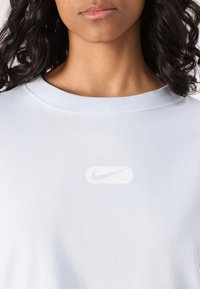 Šviesiai mėlynas medvilninis marškinėliai su apvaliu kaklu. Yra baltas Nike logotipas priekyje, lygi tekstūra ir laisvas kirpimas.