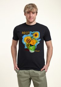 Svart t-shirt med en färgglad grafik av solrosor i en grön vas, med texten "apoh London" och "Vincent" i kontrasterande färger.