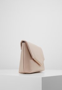 Béžová psaníčko z umělé kůže s trojúhelníkovým překlopem a kováním ve zlaté barvě. Hladká textura a minimalistický tvar, umístěné vzpřímeně.