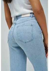 Svijetloplave traperice visokog struka, s leđnim džepovima i šivanim dizajnom. Tkanina ima glatku, blago teksturiranu završnicu.