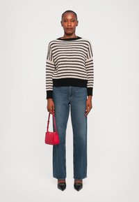 Pull en tricot noir et crème à rayures, jeans bleus à jambes larges, escarpins noirs à bout pointu, et un petit sac à main rouge. Texture lisse et coupe décontractée.