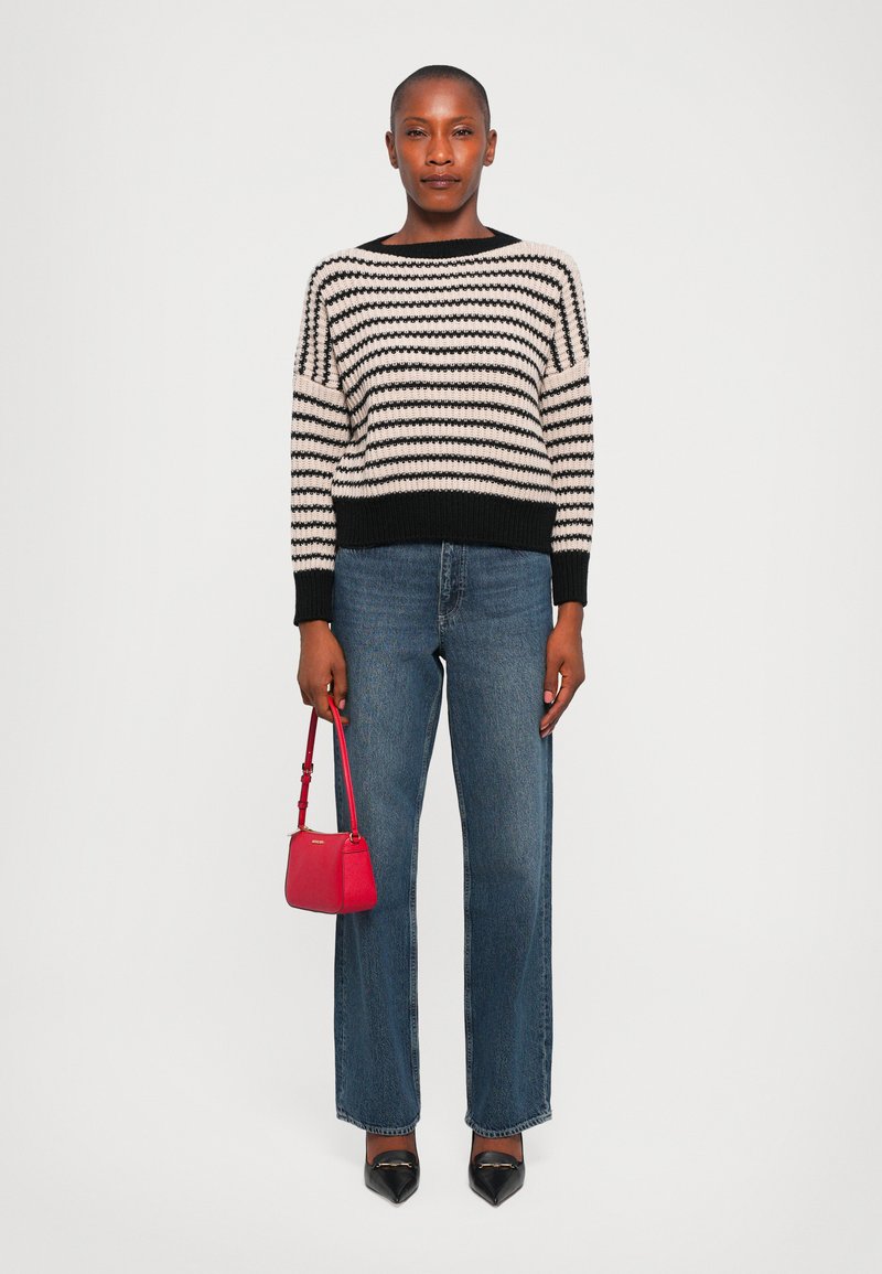 Pull en tricot noir et crème à rayures, jeans bleus à jambes larges, escarpins noirs à bout pointu, et un petit sac à main rouge. Texture lisse et coupe décontractée.