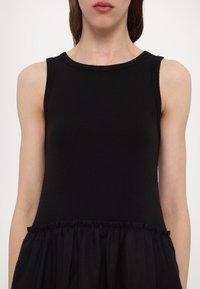 Top noir sans manches avec une texture côtelée au niveau du buste et une jupe fluide froncée à la taille. Encolure ras du cou simple.