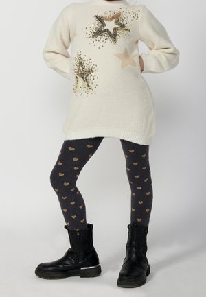 Biały sweter z złotymi gwiazdkowymi zdobieniami, zestawiony z ciemnoszarymi legginsami z wzorem złotych serc oraz czarnymi botkami za kostkę.