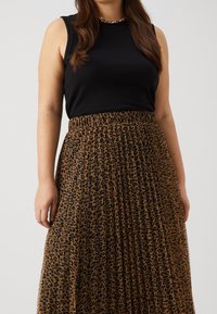 Svart ärmlös topp tillsammans med en flödande plyschkjol i brunt som har ett svart leopardmönster och ett elastiskt midjeband.