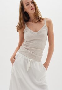 Hellgraues, geripptes Tanktop mit V-Ausschnitt und dünnen Trägern. Kombiniert mit einem weißen Rock mit Kordelzug in der Taille, beide aus weichem, leichtem Material.