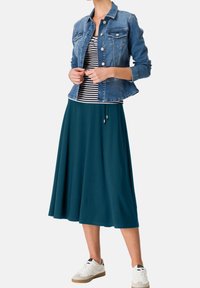 Veste en denim, haut rayé et jupe maxi bleu sarcelle. Baskets blanches avec semelles gomme. Textures lisses et design décontracté.