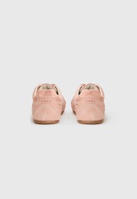 Des chaussures de sport en daim rose avec une semelle basse, présentant un design texturé, des perforations et une semelle en caoutchouc. La vue arrière montre les détails de la marque.