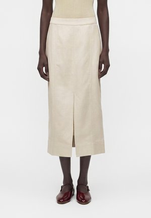 Μπεζ μίντι φούστα με εμπρόσθια σχισμή, φορεμένη με μπορντό παπούτσια Mary Jane και κρεμ ριμπζαριστό αμάνικο τοπ, εμφανίζεται από το μέσο του κορμού μέχρι τα πόδια.