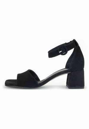 Sandalias de tacón de ante negro con una amplia correa frontal, una correa en el tobillo y un tacón cuadrado. Textura suave con un diseño minimalista.