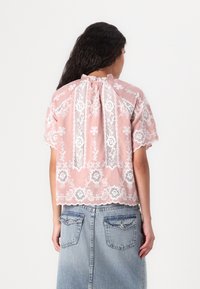 Vaaleanpunainen lyhythihainen pusero, jossa on kukallinen pitsikoristelu, röyhelöinen pääntie ja aallotetut reunat, yhdistetty farkkuhameeseen.