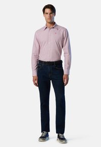 Camisa de rayas rojas y blancas con botones combinada con jeans de color azul oscuro. El conjunto incluye un cinturón negro y zapatillas deportivas con detalles en gris.