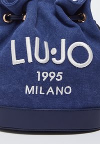 Temno modra platnena torba na vezanje, ki ima belo vezeno besedilo "LIU·JO 1995 MILANO" ter zlate kovinske dodatke na odprtini.