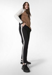 Bruin en wit color-blocked langwerpige top, gecombineerd met zwarte broek met zijwitte strepen, gedragen met zwarte sneakers.