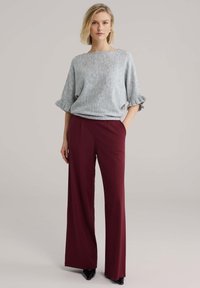 Pull gris clair texturé avec des poignets retroussés, associé à un pantalon large bordeaux. Une paire de chaussures noires pointues complète la tenue.