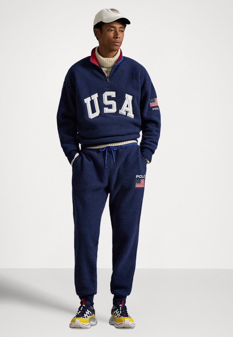 Polaire marine avec inscription "USA", col zippé et finitions côtelées ; pantalon assorti avec logos brodés et tissu texturé.
