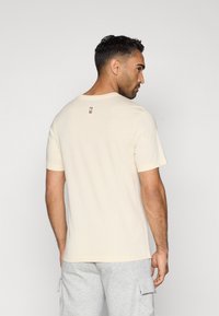 Krémové tričko s krátkym rukávom a okrúhlym výstrihom, hladká textúra a malé logo na chrbte. Voľný strih a jednoduchý dizajn.