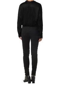 Black satin blouse with a high collar and buttoned cuffs, paired with black skinny jeans and heeled ankle boots. Simple, tailored design.