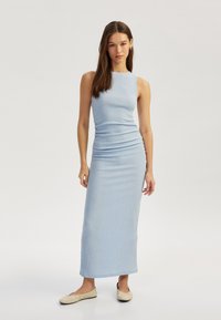 Helles blaues, ärmelloses Maxikleid aus strukturierter Stoff, taillierte Silhouette und kniehoher Schlitz an der Seite, kombiniert mit beigen Ballerinas.