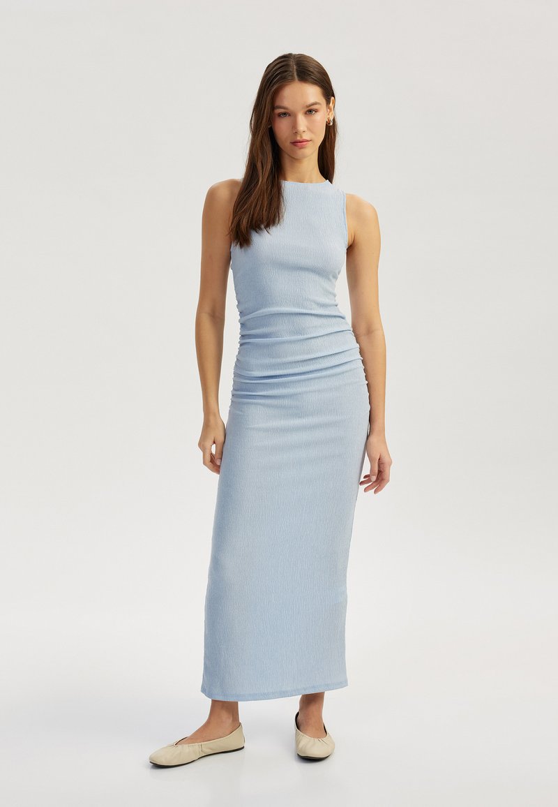 Helles blaues, ärmelloses Maxikleid aus strukturierter Stoff, taillierte Silhouette und kniehoher Schlitz an der Seite, kombiniert mit beigen Ballerinas.