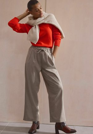 Pull en tricot rouge, écharpe beige surdimensionnée et pantalons légers à jambes larges gris clair avec une taille élastique. Bottines à talons carrés marron.
