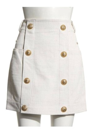 Mini-jupe blanche texturée à taille haute, avec deux poches latérales et deux rangées verticales de boutons décoratifs dorés.