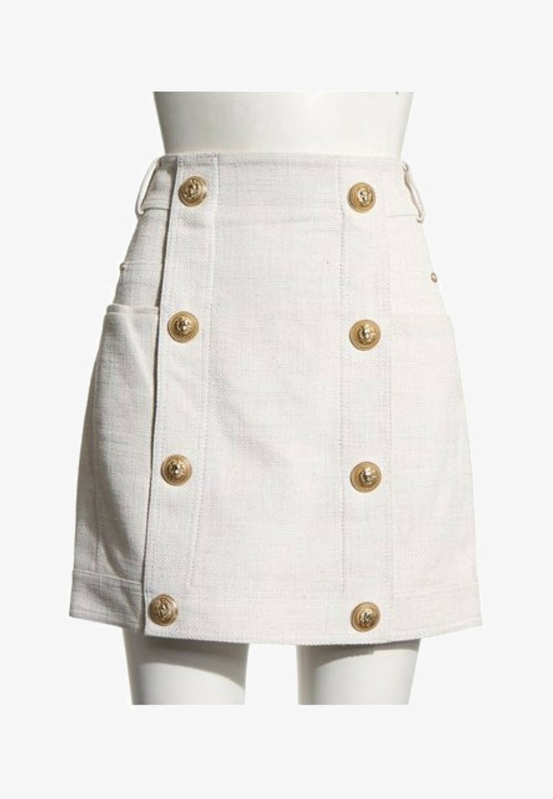 Mini-jupe blanche texturée à taille haute, avec deux poches latérales et deux rangées verticales de boutons décoratifs dorés.