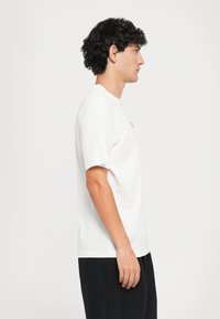Hvit bomulls T-skjorte med rund hals og korte ermer. Enkelt design med løs passform, kombinert med svarte shorts.