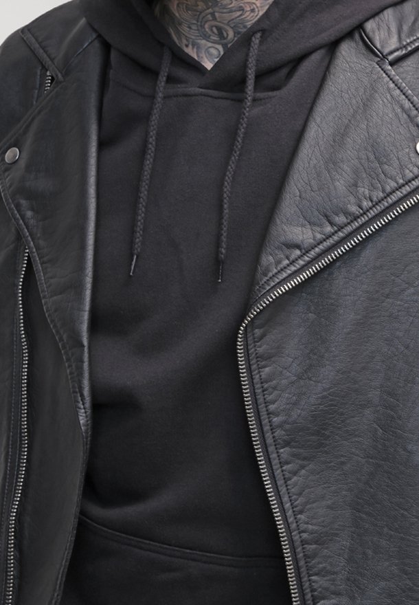 Blouson motard en cuir noir avec zips argentés porté sur un sweat-shirt noir à capuche avec cordon de serrage et texture douce, mettant en avant un style superposé.