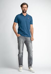 Camisa polo azul de manga corta con cuello, combinada con jeans gris claro. Zapatillas blancas de tipo slip-on. Diseño sencillo, sin patrones visibles.