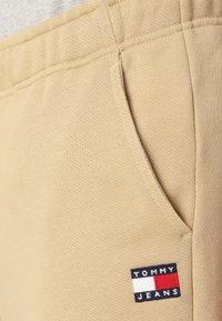 Bežové bavlněné jogger kalhoty s textura, obsahující boční kapsu a nášivku loga Tommy Jeans v námořnické modré, bílé a červené barvě.