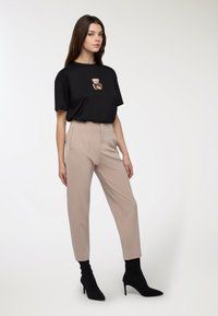 Czarny t-shirt z grafika niedźwiedzia; beżowe dopasowane spodnie; model w czarnych skarpetkowych botkach; minimalistyczny design i czyste linie.