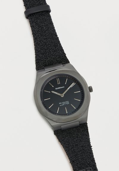 Στρογγυλό μαύρο ρολόι χειρός D1 Milano με ασημί δείκτες ώρας, λεπτό και ώρα, και υφασμάτινο μαύρο λουράκι με υφή.