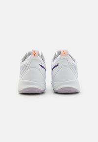 Vita sportskor i vitt med en slät yta, lila accenter nära hälen och orange logotyp på dragfliken bak.