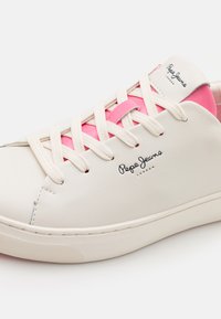 Hvide lædersneakers med rosa accenter, der har rundt tå, gummisål og beige snørebånd. Branded logo på siden.