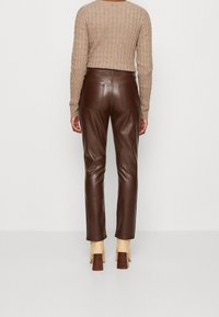 Pantalones de cuero marrón con una textura suave, corte slim, bolsillos traseros, combinados con zapatos de tacón color beige y un top de punto beige texturizado.