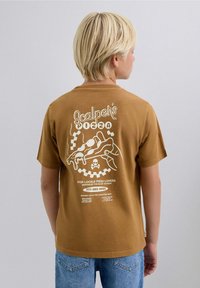Brown cotton t-shirt featuring white graphic design on the back of a pizza slice, skull, and text. Short sleeves and relaxed fit.