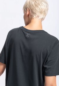 Steenkoolgrijze t-shirt met korte mouwen en een ronde halslijn; heeft een kleine, lichtgrijze schaarafbeelding op de achterkant bij de hals.