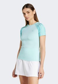 Svijetloplava sportska majica kratkih rukava s okruglim izrezom. Ima tri pruge na ramenima i logo na prsima. Glatka tekstura.