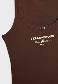 Hnědý tílko s kulatým výstřihem, krajkovým zdobením a malým květinovým akcentem. Na přední straně je vytištěno "YELLOWSTONE", "Dutton Ranch" a text s místem.
