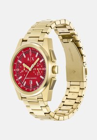 Zlatni nehrđajući čelični sat s okruglim crvenim brojčanikom, bijelim oznakama sati i metalnom narukvicom na karike. Ima prikaz datuma i kronografske podbrojeve.