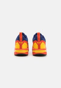 Zapatos deportivos con parte superior de malla en azul, talón rojo y acentos amarillos. Cuenta con un collar acolchado y una suela de goma texturizada para mayor agarre.