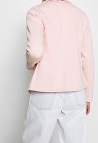 Ljusrosa fleecejacka med skräddarsydd passform, med krage och sömdetaljer, kombinerad med ljusa denimbyxor.