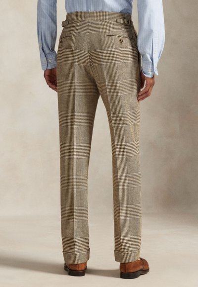 Mann trägt maßgeschneiderte, braun-beige karierte Hose, kombiniert mit polierten braunen Lederschuhen und einem hellblauen Hemd.