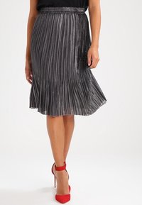 Metaliczna plisowana spódnica midi w ciemnoszarym kolorze, z marszczonym pasa i falującym dołem. W połączeniu z czerwonymi szpilkami.