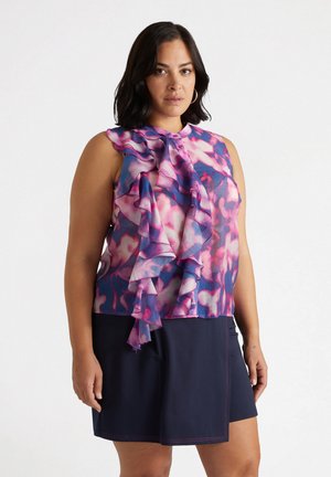 Blouse à fleurs avec dos enroulé et devant volanté, présentant des teintes de rose et de bleu. Associée à une jupe bleu marine foncé, affichant une texture lisse et un style simple.