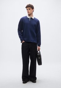 Μπλε ναυτική μπλούζα με λευκό γιακά, μακριά μανίκια και άνετη εφαρμογή, σε συνδυασμό με παντελόνι από σκούρο τζιν με φαρδιά μπατζάκια και μαύρη τσάντα.