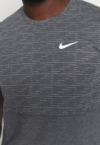 Męska szara koszulka sportowa wykonana z teksturowanej tkaniny, z okrągłym dekoltem i małym białym logo Nike na górnej lewej części klatki piersiowej.