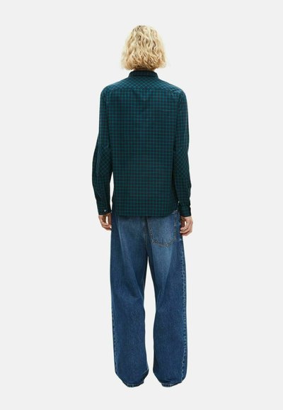 Camicia button-up di colore verde scuro con motivo a quadri, dotata di maniche lunghe e colletto aperto, abbinata a jeans in denim blu a vestibilità ampia.