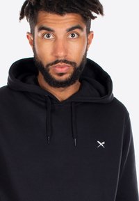 Felpa nera con cappuccio in cotone misto, dotata di un cappuccio regolabile e di un piccolo logo ricamato sul petto. Texture liscia e vestibilità rilassata.